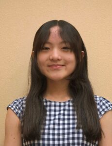 Picture of a young female with long dark hair, wearing a blue and white checked short sleeved top.