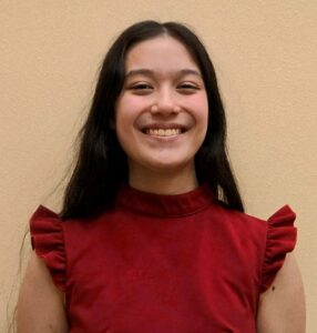 Picture of a young female with long dark hair, wearing a red top with short ruffled sleeves.
